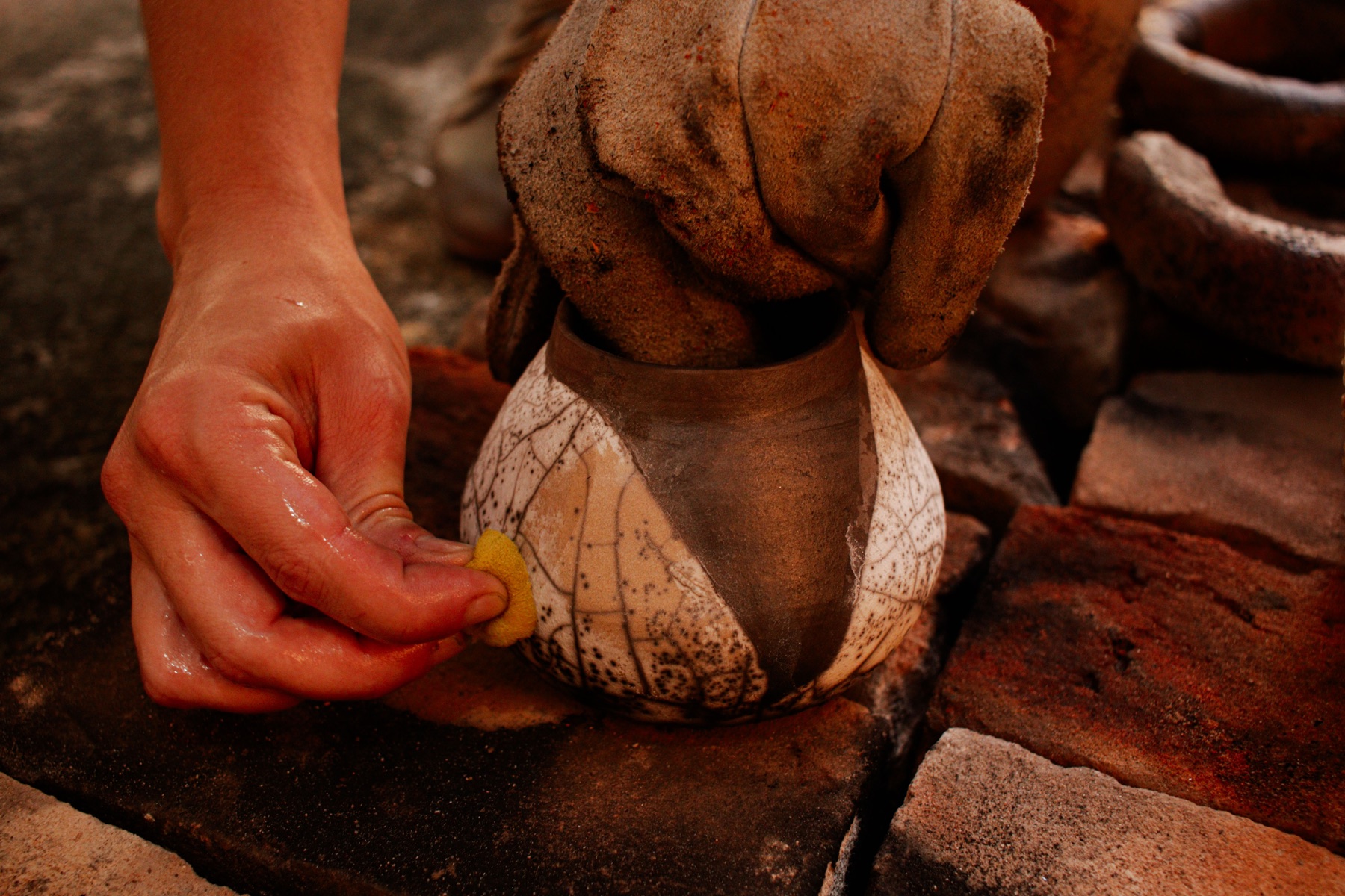 Mãos finalizando uma peça durante uma queima artesanal